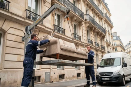 Deux déménageurs professionnels installant un monte-meubles sur la façade d'un immeuble haussmannien pour déménager un canapé